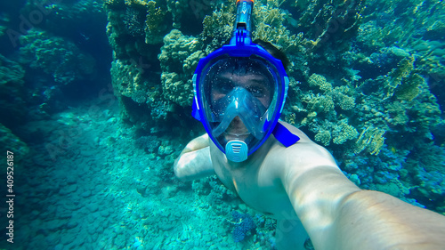 a young diver wearing an underwater mask takes a selfie at the bottom of the blue sea