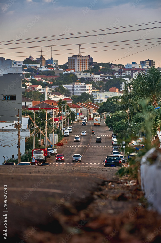 Avenue, showing the city in the background, in warm tones of yellow, with contrasting blue sky, and vegetation - Avenida Tuparendi, Santa Rosa, Rio Grande do Sul, Brasil.