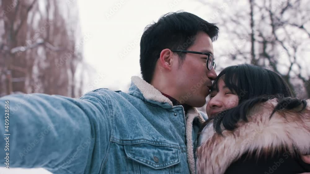Happy young couple hugging and taking selfie in the snow covered park. Winter season. High quality 4k footage