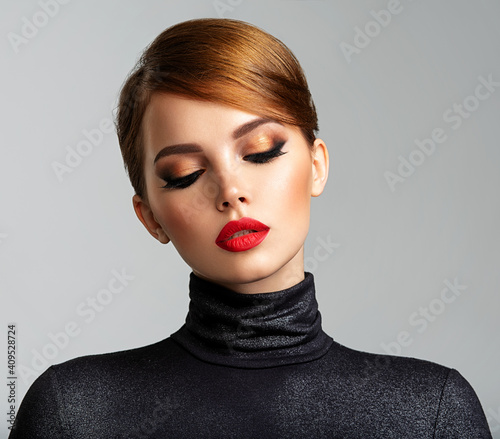 Beautiful girl with red lips and short hair. Pretty face of an young sensual woman. Closeup portrait of a model with bright makeup on a face. Attractive female posing at studio  in black closes.