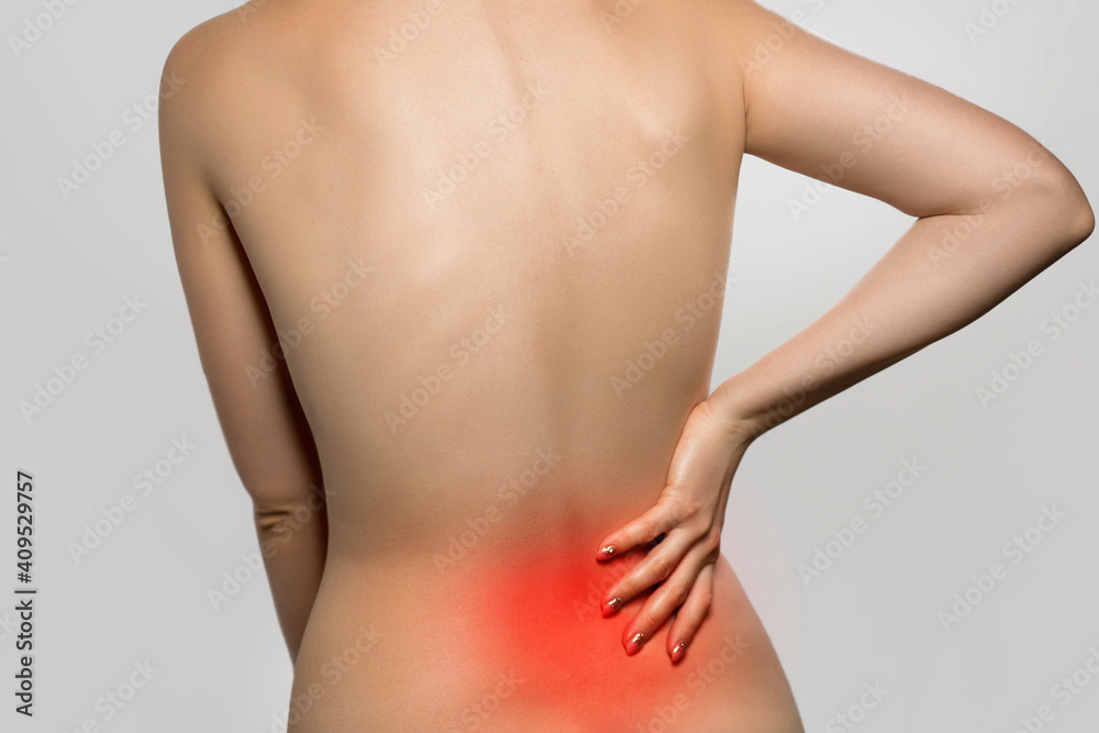 Naklejka premium Woman having backache, pain back isolated on gray background. Scoliosis. Spinal cord problems on womans back. Beautiful naked woman touching her back.