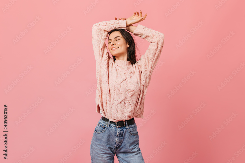 Portrait of charming girl with pleasure posing with arms raised. Woman in knitted sweater and mom jeans smiling with eyes closed Portrait of charming girl with pleasure posing with arms raised. Woman in knitted sweater and mom jeans smiling with eyes closed