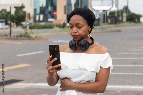 Unsmiling African woman taking a selfie with a smartphone with black headphones.