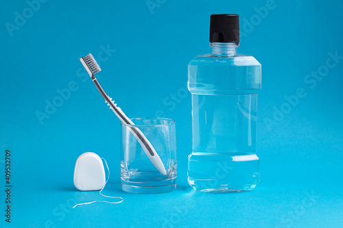 A toothbrush in a glass, mouthwash and dental floss on a blue background. Oral hygiene, daily care.