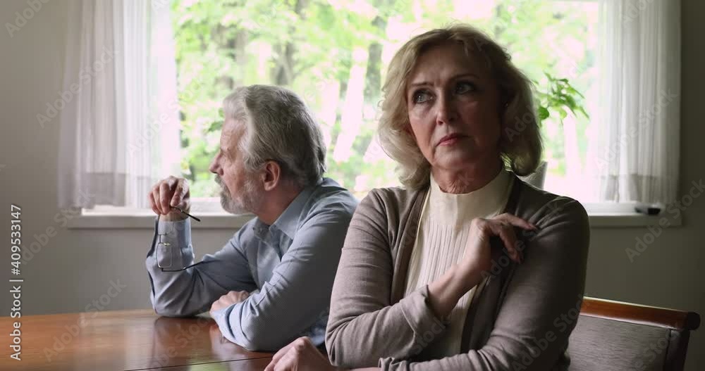 Stressed middle aged family couple sitting separately, ignoring each other after misunderstanding quarrel, having marriage relationship problems. Unhappy older husband and wife suffering from conflict Stressed middle aged family couple sitting separately, ignoring each other after misunderstanding quarrel, having marriage relationship problems. Unhappy older husband and wife suffering from conflict