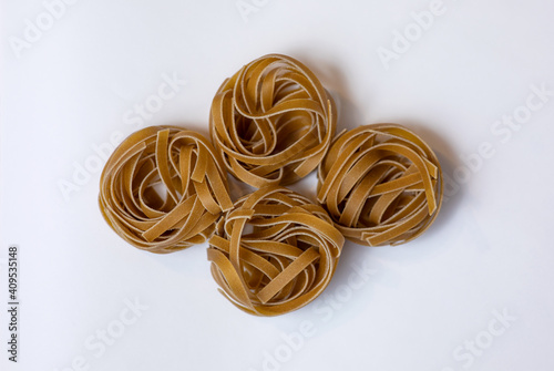 Raw whole grain brown pasta Tagliatelle on a white background, made with wheat flour, rich in nutrients: protein, carbohydrates and fiber