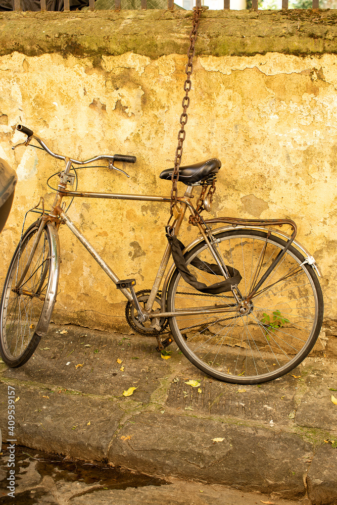 Old bicycle chained up securely to metal work on a wall in a side street Old bicycle chained up securely to metal work on a wall in a side street