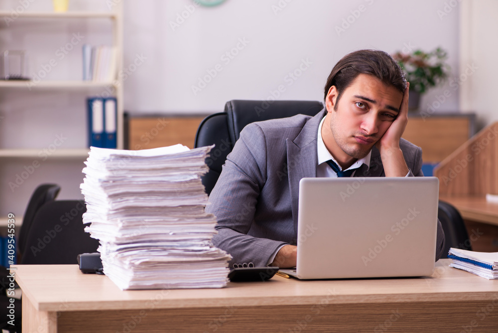 Young male employee unhappy with excessive work in the office Young male employee unhappy with excessive work in the office