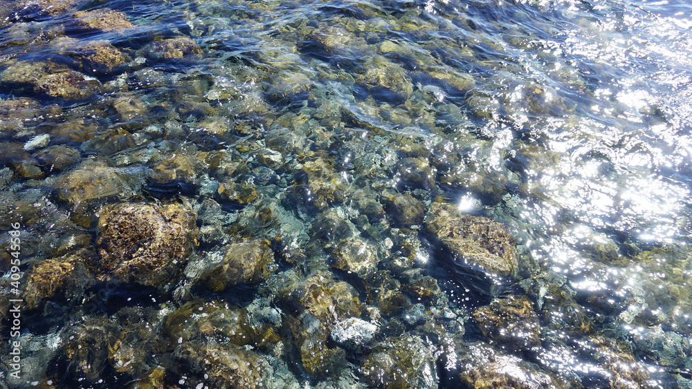 Transparent ocean water shining in the sun. Pebble bottom below crystal clear water.       