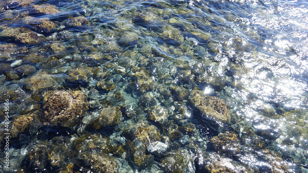 Transparent ocean water shining in the sun. Pebble bottom below crystal clear water. Transparent ocean water shining in the sun. Pebble bottom below crystal clear water.