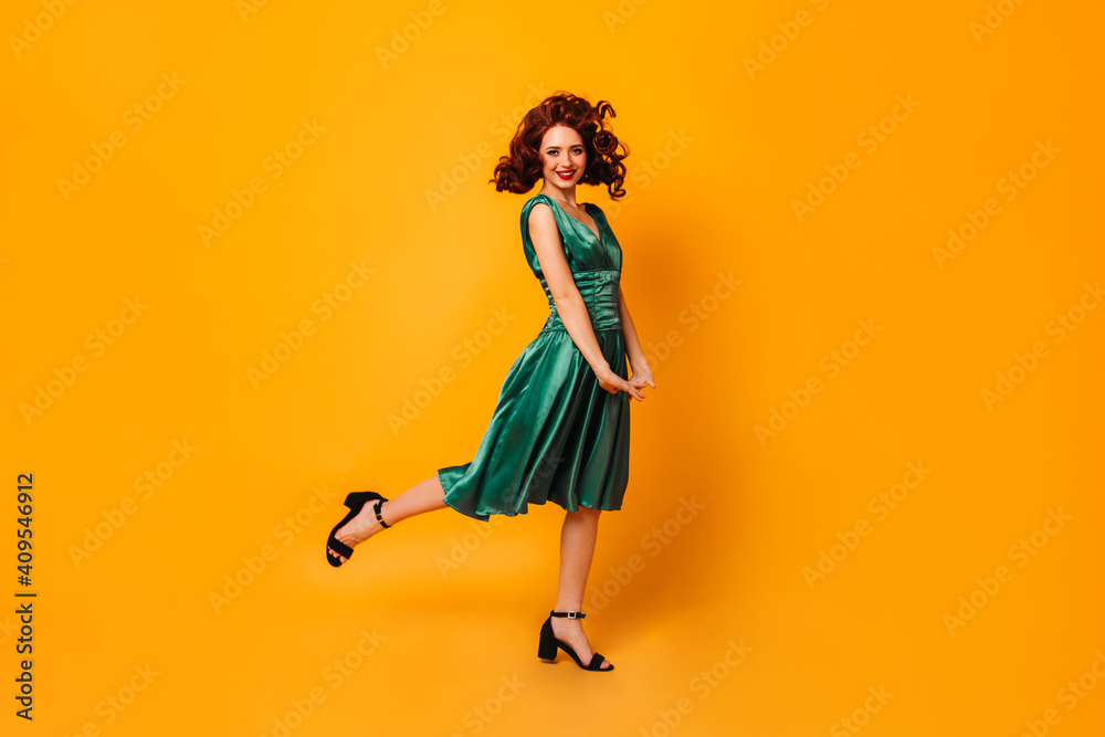 Excited fit girl in green dress standing on one leg. Full length view of graceful lady dancing on yellow background. - obrazy, fototapety, plakaty 