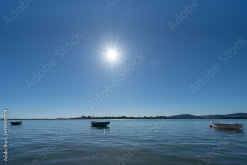 Small dinghies afloat on calm water as sun bursts overhead.
