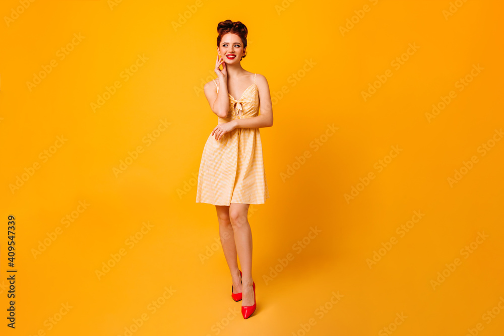 Full length view of cheerful pinup lady. Attractive young woman in dress standing on yellow background. Full length view of cheerful pinup lady. Attractive young woman in dress standing on yellow background.