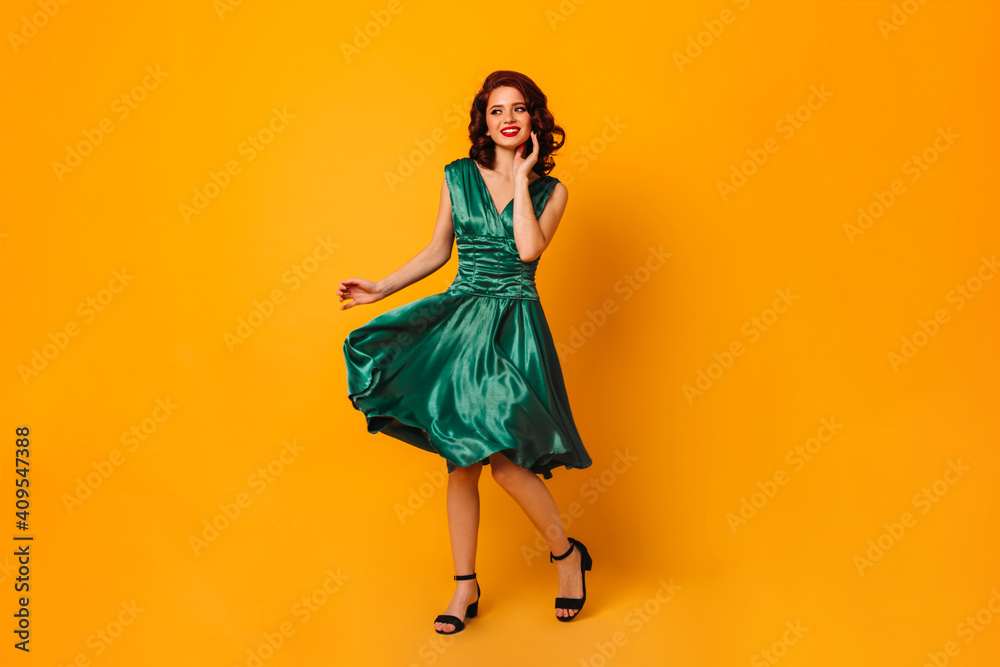 Charming woman in green dress smiling and looking away. Full length view of gorgeous curly girl dancing on yellow background. - obrazy, fototapety, plakaty 