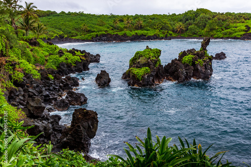 Black lava rock sea stacks sit in blue water just beyond the black sand beach of Waiʻanapanapa State Park in Hana on the island of Maui, Hawaii, United States.