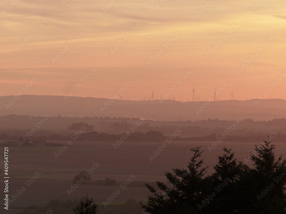 Rosa-Gelb gefärbte Felder und Landschaften mit Windrädern am Horizont in der Abenddämmerung Rosa-Gelb gefärbte Felder und Landschaften mit Windrädern am Horizont in der Abenddämmerung