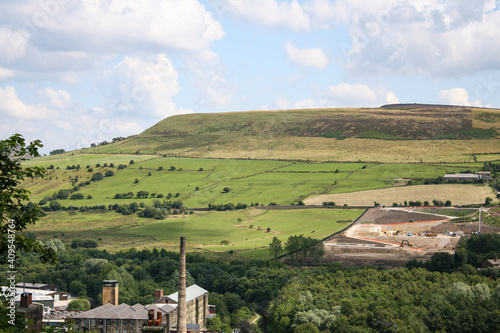 Mossley, England - A green hill and valley with a mill in front of them on the outskirts of Mossley on a summer day.  Image has copy space.