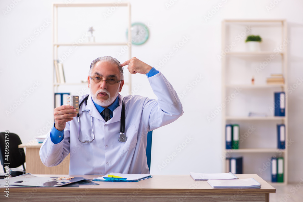 Old male doctor writing prescription in the clinic Old male doctor writing prescription in the clinic