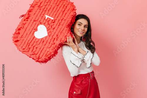 Blue-eyed woman is smiling affably and holding like sign on pink background. Lady in red skirt posing in great mood photo