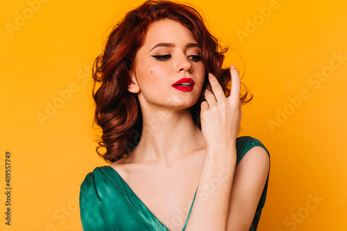 Sensual caucasian girl touching wavy hair. Studio shot of ginger young woman in green attire.