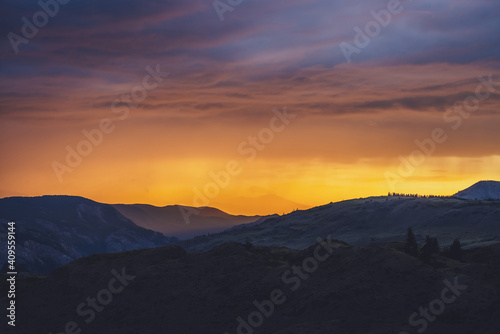 Atmospheric landscape with silhouettes of mountains with trees on background of vivid orange blue violet dawn sky. Colorful nature scenery with sunset or sunrise of illuminating color. Sundown paysage © Daniil