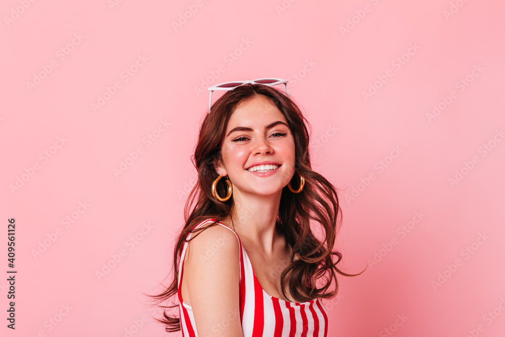 Dark-haired curly girl with glasses smiling. Portrait of lady in striped top on pink background Dark-haired curly girl with glasses smiling. Portrait of lady in striped top on pink background