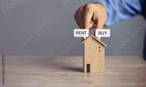 Business hand holding home with Buy or Rent, copy space. Property investment and house mortgage financial concept, Hand putting money coin stack with wooden house.