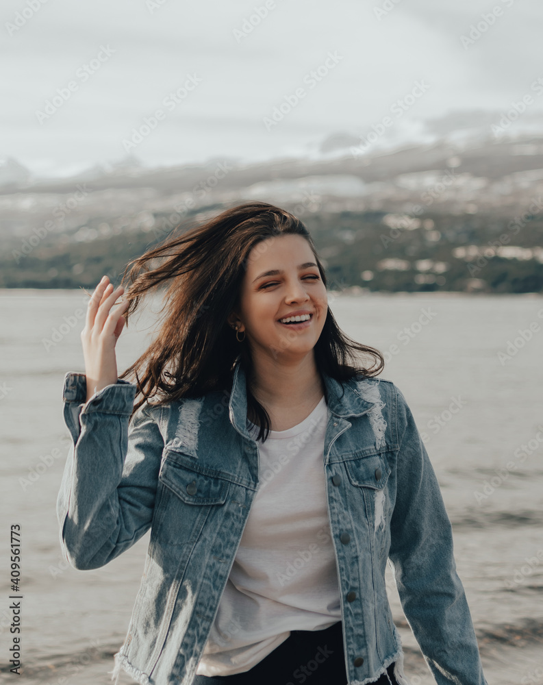 portrait of a beautiful young girl with blue jacket smiling and touching his hair at sunrise portrait of a beautiful young girl with blue jacket smiling and touching his hair at sunrise