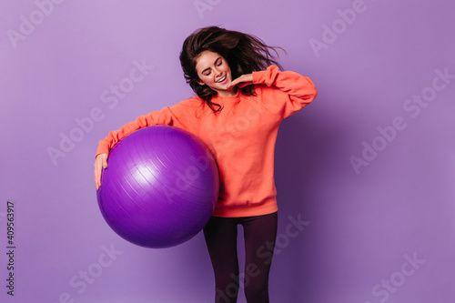 Slender lady holds huge fitball. Woman in sport outfit smiling on isolated background