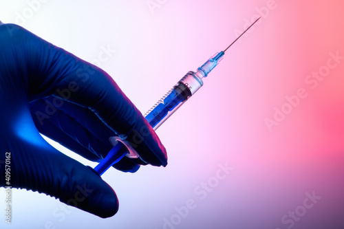 The Coronavirus Vaccine and Syringe injection in the hand in a medical glove on a pink gradient background. The concept of protection against Coronavirus infection. Healthcare and medical concept. .