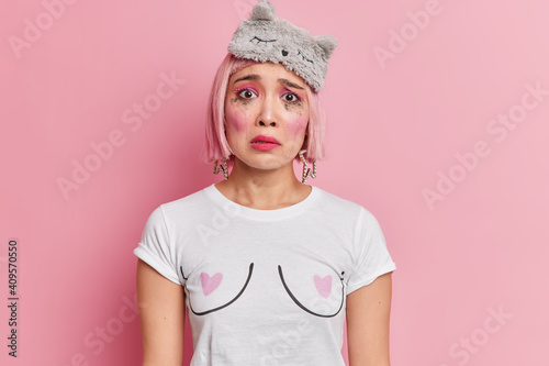 Headshot of sorrowful worried woman sobs after crying has hurt feelings looks sadly at camera spoiled makeup pink bob hair suffers after break up dressed in casual clothes dejected after date