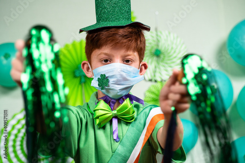 young kid with medical face mask dancing by holding pom pom on decorated background at home during saint Patrics day celebration - concept of new normal festive due to coronvirus covid-19 pandemic. photo