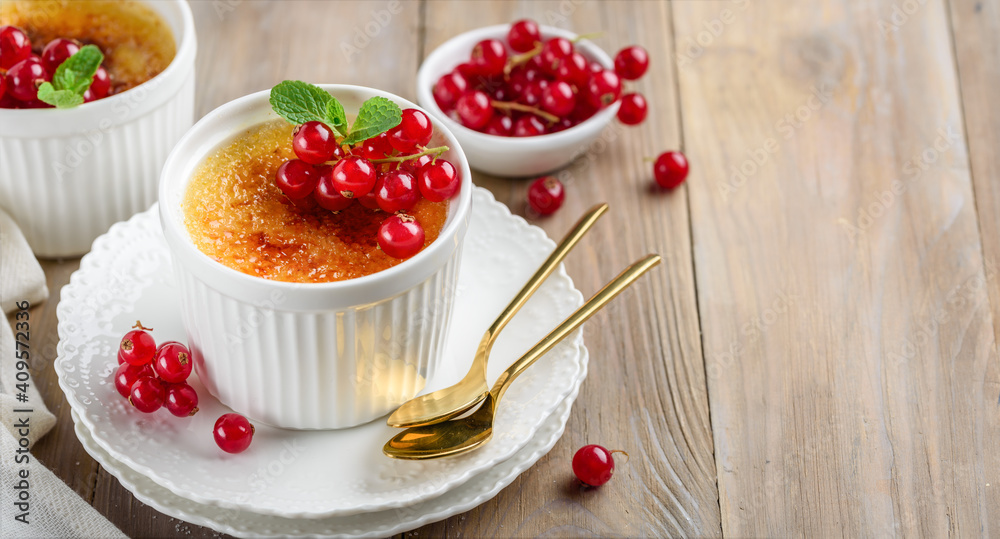 Creme brulee decorated with red currant and mint. Traditional french vanilla cream dessert with caramelised sugar. Selective focus. Copy space