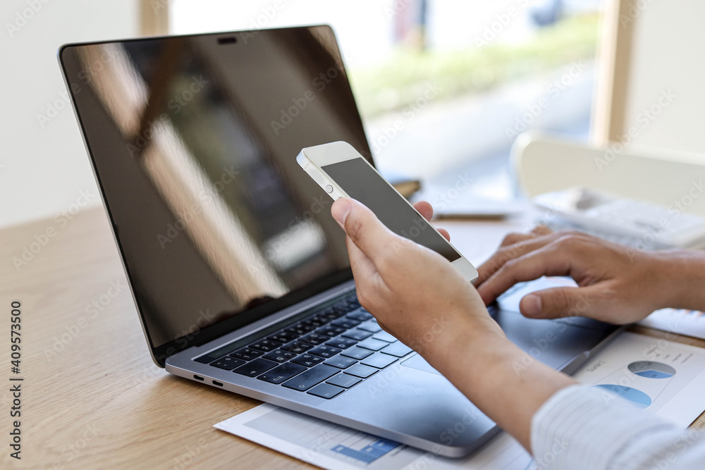 Fototapeta premium A man with a mobile phone And use the laptop. He was using a laptop to look at the mobile phone in his left hand.