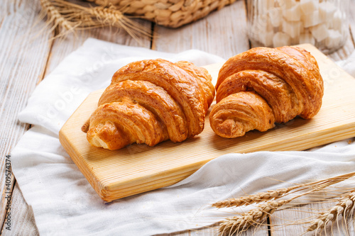 Two french croissants on the wooden cutting board decorated with wheat and napkin