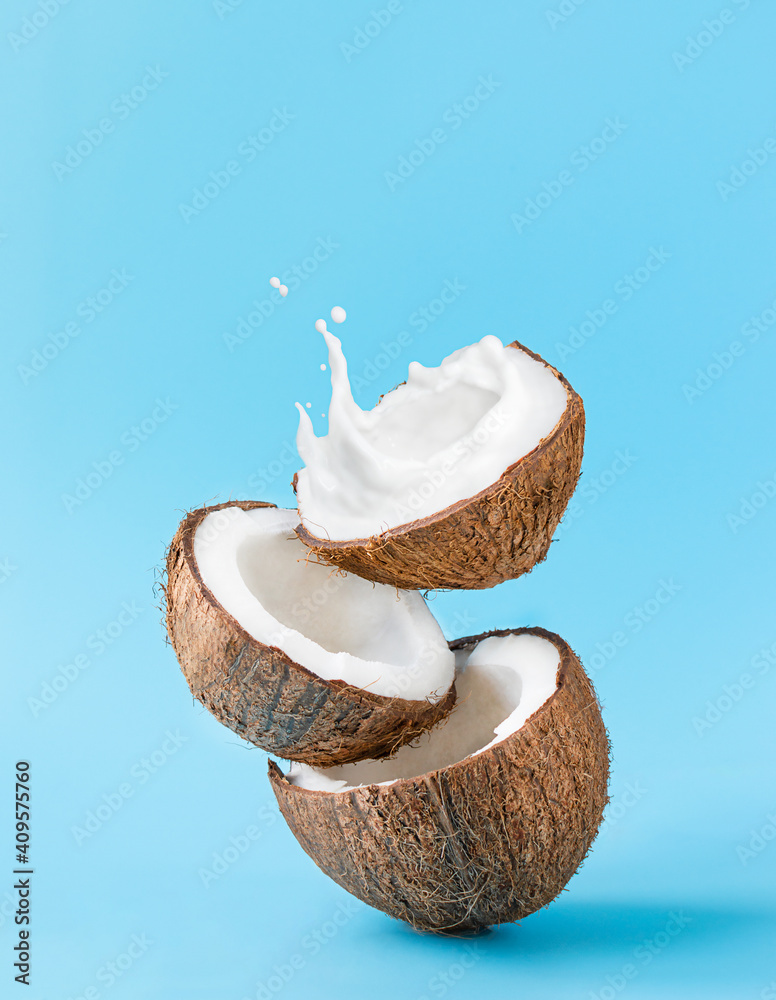 Cracked coconut with splashes of milk on blue background - obrazy, fototapety, plakaty 