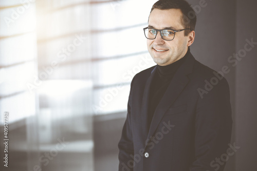 Portrait of a friendly middle aged businessman in a dark blue suit, standing straight in a sunny office. Concept of success in ba usiness nowadays © cameravit