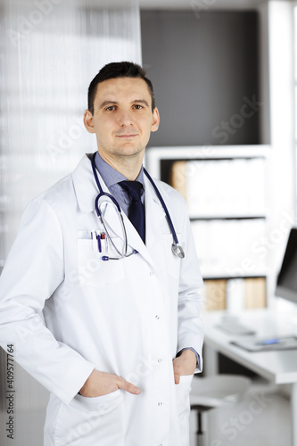 Male doctor standing straight in clinic near his working place. Perfect medical service in hospital. Medicine and healthcare concept