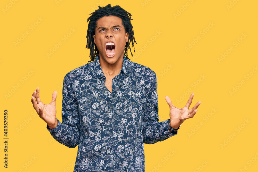 Young african american man wearing 80s shirt crazy and mad shouting and yelling with aggressive expression and arms raised. frustration concept. Young african american man wearing 80s shirt crazy and mad shouting and yelling with aggressive expression and arms raised. frustration concept.