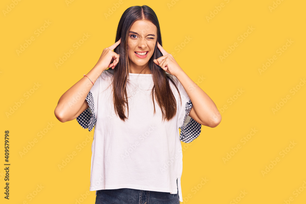 Young hispanic woman wearing casual clothes covering ears with fingers with annoyed expression for the noise of loud music. deaf concept. Young hispanic woman wearing casual clothes covering ears with fingers with annoyed expression for the noise of loud music. deaf concept.