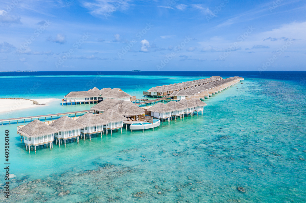 Aerial view of Maldives island, luxury water villas resort and wooden pier. Beautiful sky and ocean lagoon beach background. Summer vacation holiday and travel concept. Paradise aerial landscape pano