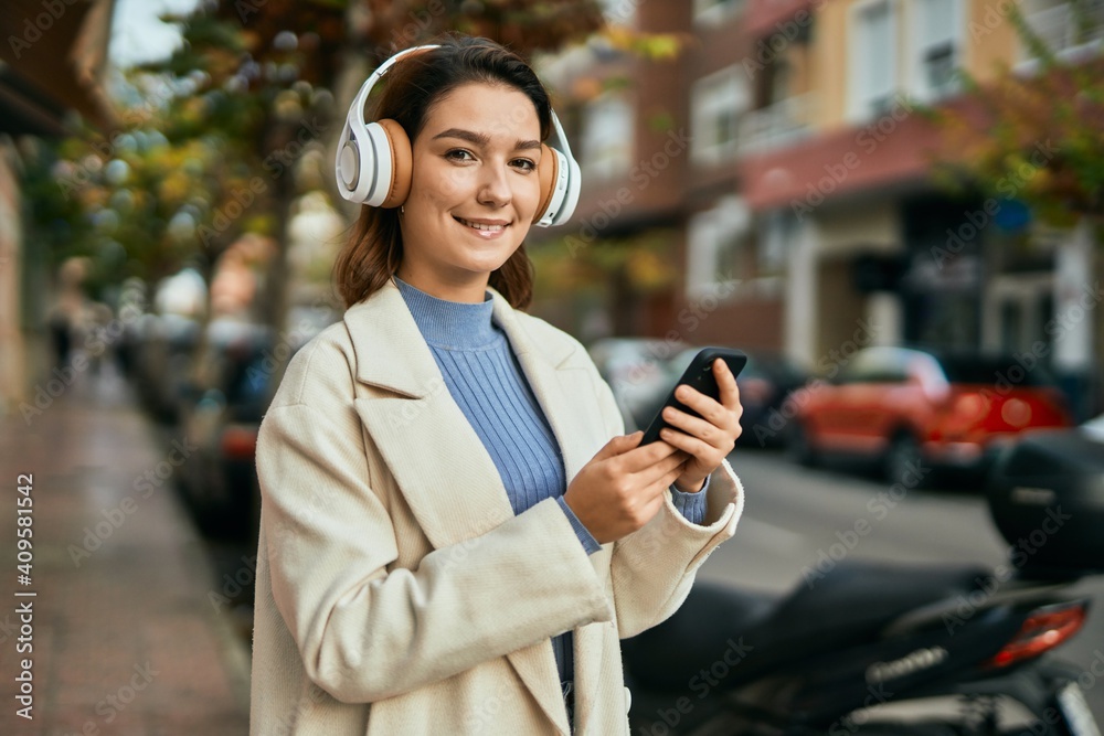 Young hispanic woman smiling happy using smartphone and headphones at the city.