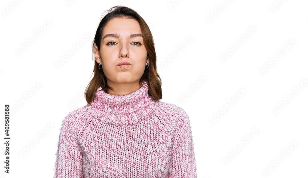 Young caucasian girl wearing wool winter sweater puffing cheeks with funny face. mouth inflated with air, crazy expression. Young caucasian girl wearing wool winter sweater puffing cheeks with funny face. mouth inflated with air, crazy expression.