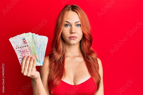 Young redhead woman holding hong kong dollars banknotes thinking attitude and sober expression looking self confident