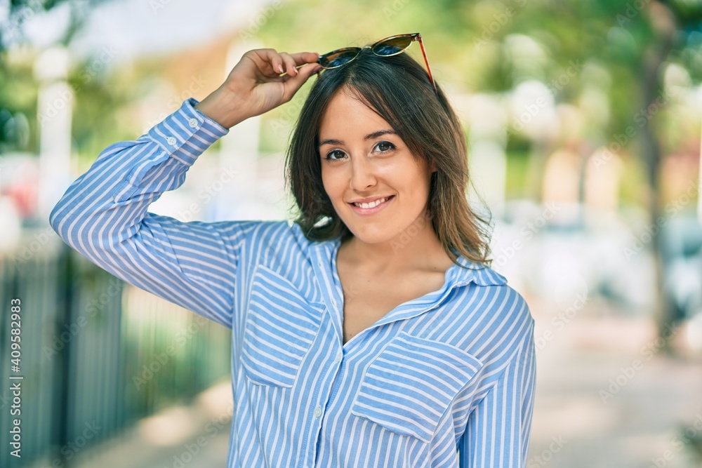 Young hispanic woman smiling happy touching her sunglasses at the park.