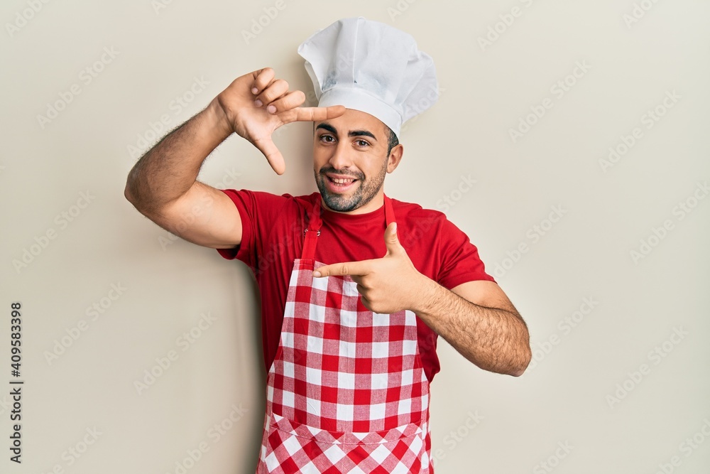 Young hispanic man wearing baker uniform smiling making frame with hands and fingers with happy face. creativity and photography concept. Young hispanic man wearing baker uniform smiling making frame with hands and fingers with happy face. creativity and photography concept.
