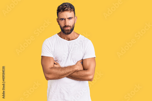 Young hispanic man wearing casual white tshirt skeptic and nervous, disapproving expression on face with crossed arms. negative person.