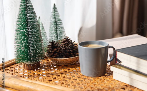 A cup of coffee, books, small pine tress and pine cones on wooden table at home