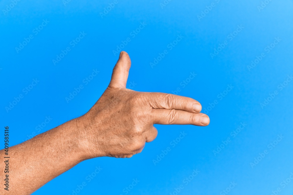 Hand of senior hispanic man over blue isolated background gesturing fire gun weapon with fingers, aiming shoot symbol Hand of senior hispanic man over blue isolated background gesturing fire gun weapon with fingers, aiming shoot symbol