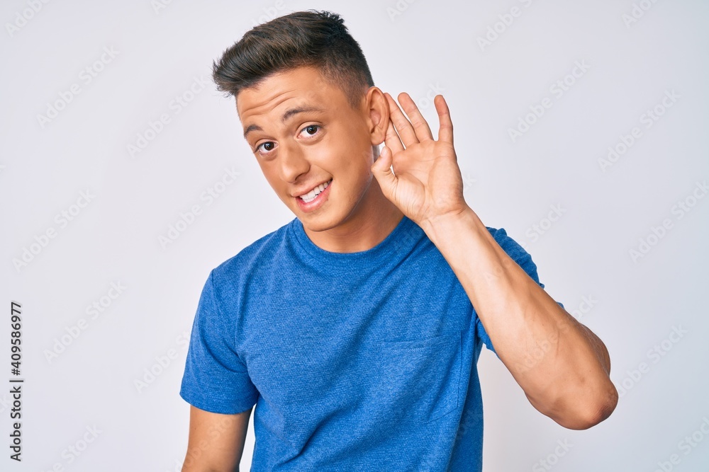 Young hispanic boy wearing casual clothes smiling with hand over ear listening and hearing to rumor or gossip. deafness concept. Young hispanic boy wearing casual clothes smiling with hand over ear listening and hearing to rumor or gossip. deafness concept.
